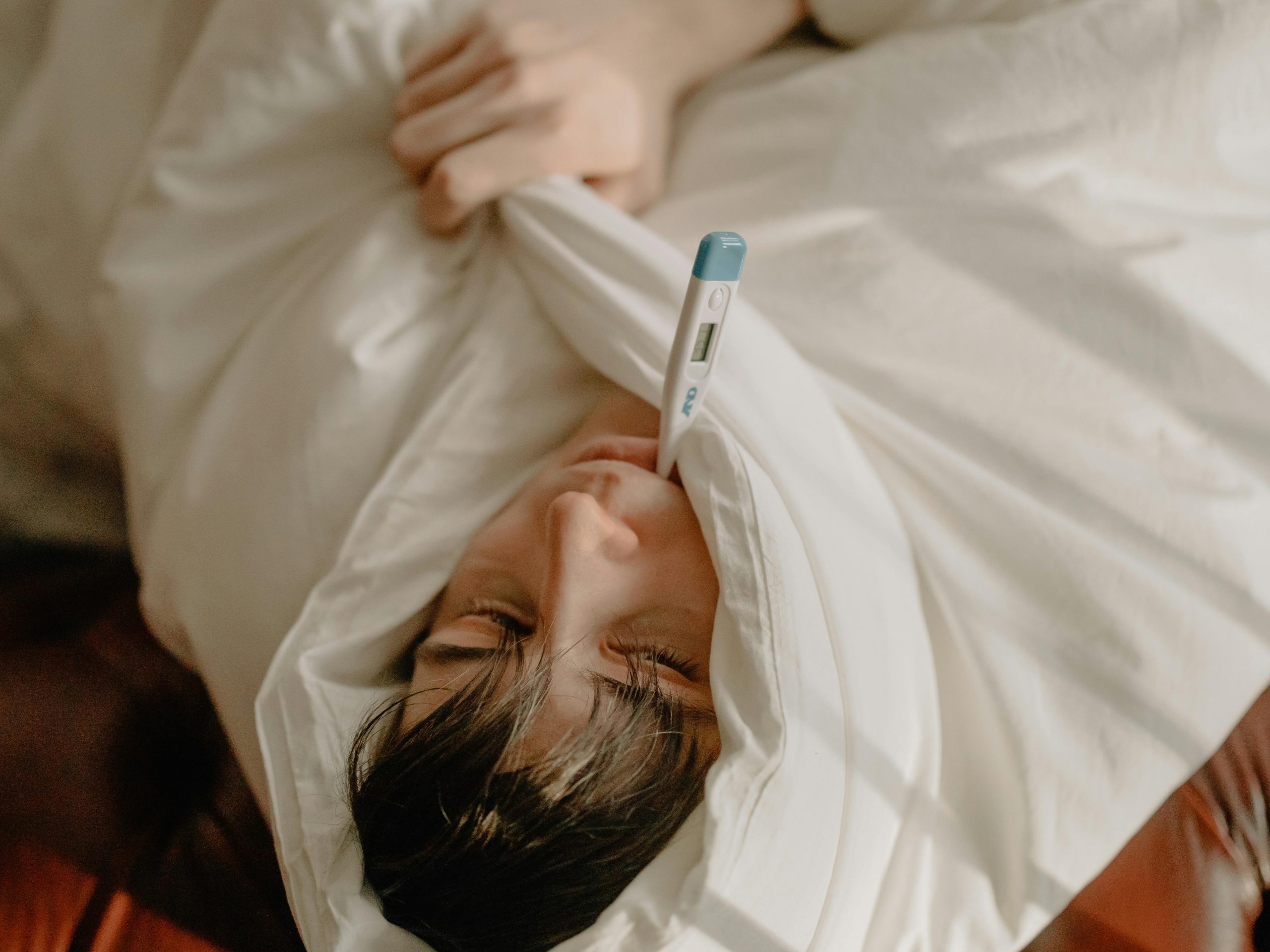 man covered in a blanket with a thermometer in his mouth