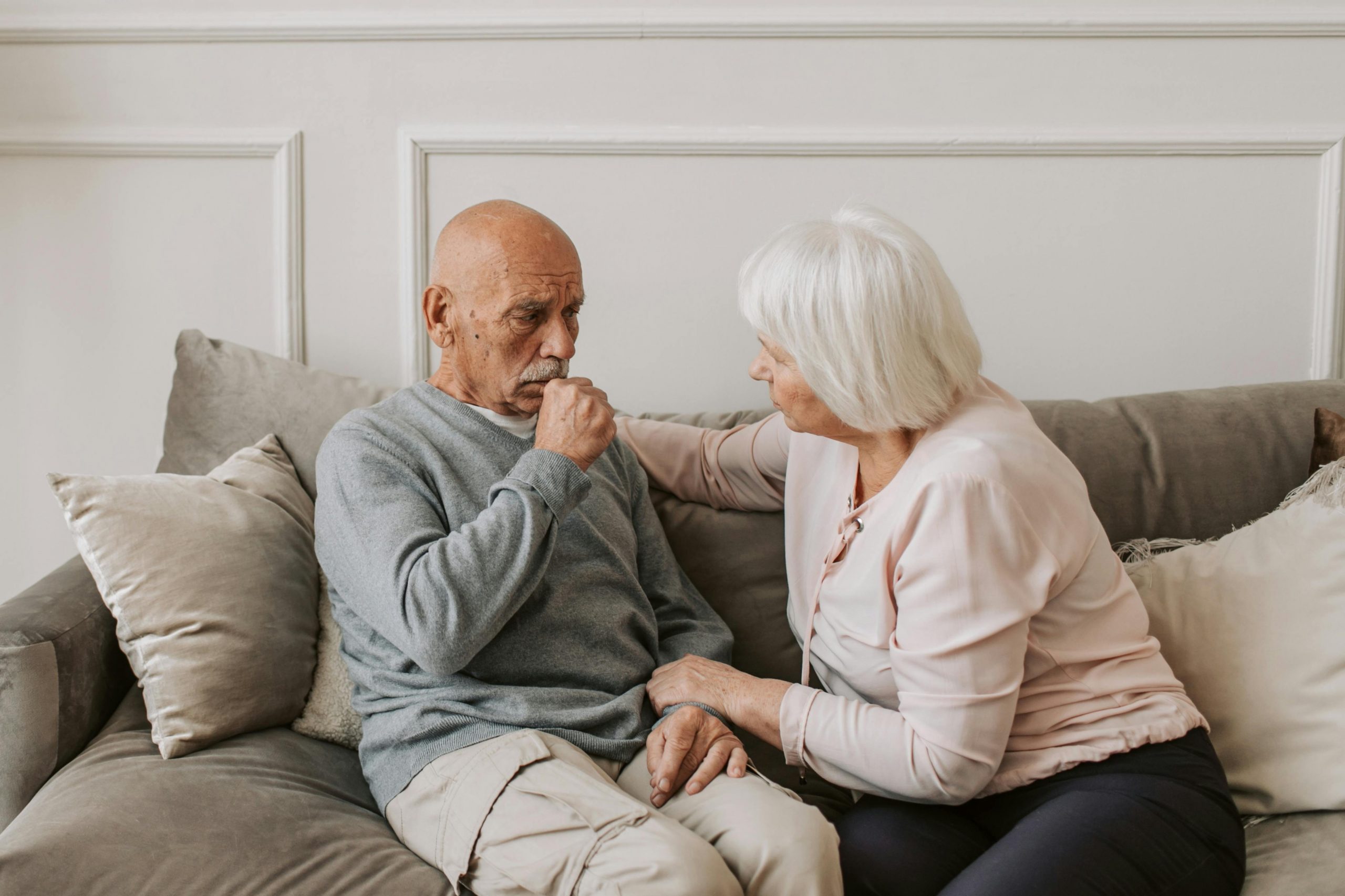 elderly man coughing while an elderly woman tends to him